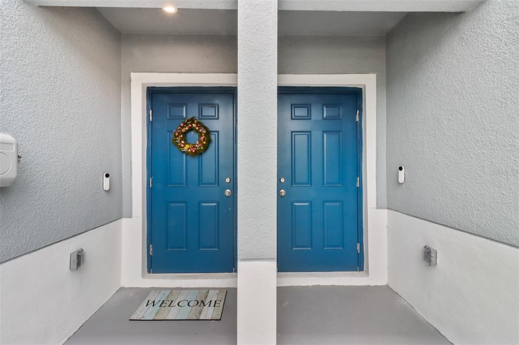 Two blue front doors with a welcome mat sit side-by-side on a gray porch — 3138 VICTORIA INLET DRIVE, HOLIDAY, FL