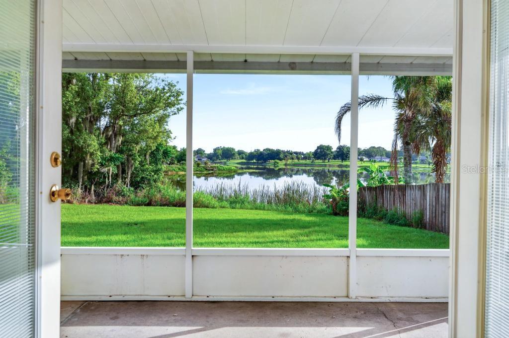 A screened-in porch overlooks a grassy backyard and a lake with trees in the distance — 57 CAYMAN CIRCLE, UMATILLA, FL