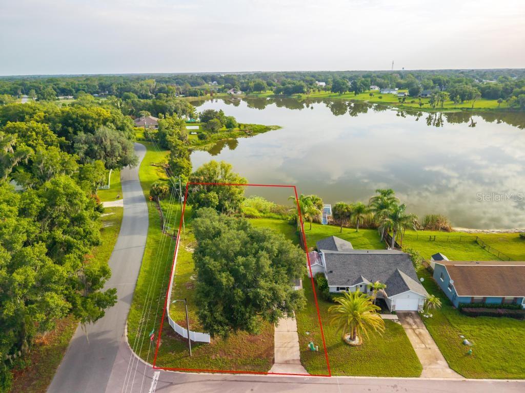 An aerial view shows a residential lot with a house and driveway bordering a lake — 57 CAYMAN CIRCLE, UMATILLA, FL