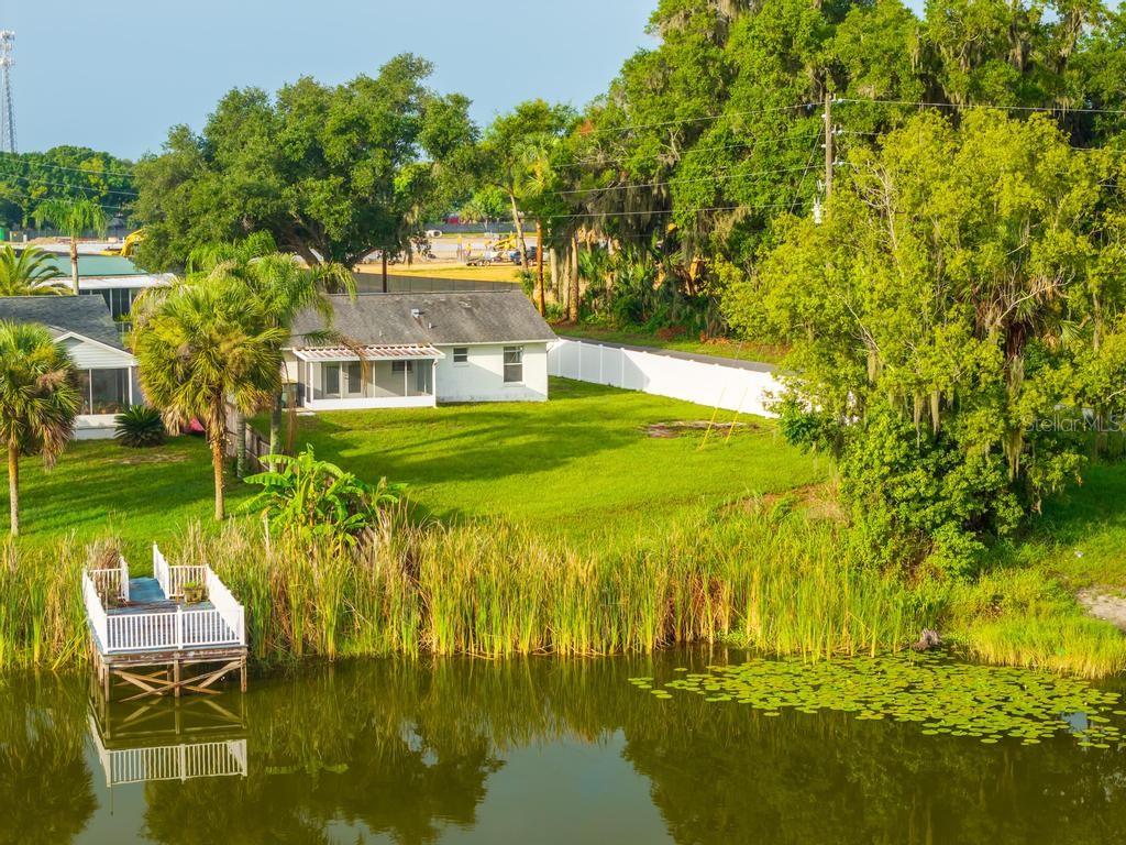 An exterior view of a white house with a backyard, dock, and pond — 57 CAYMAN CIRCLE, UMATILLA, FL