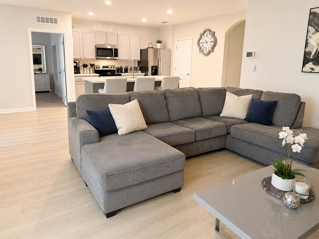 A gray sectional sofa sits in a living room facing an open-concept kitchen with white cabinets — 3653 SCARLET OAK DRIVE, ST CLOUD, FL