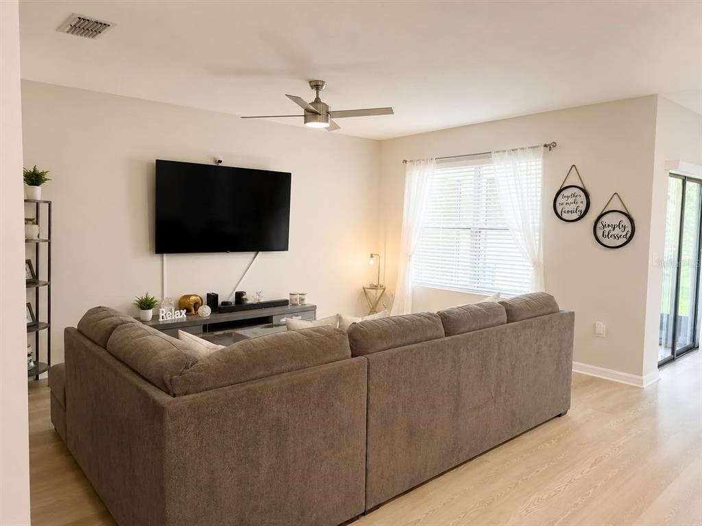 A living room features a large sectional sofa, a wall-mounted television, and light wood flooring — 3653 SCARLET OAK DRIVE, ST CLOUD, FL