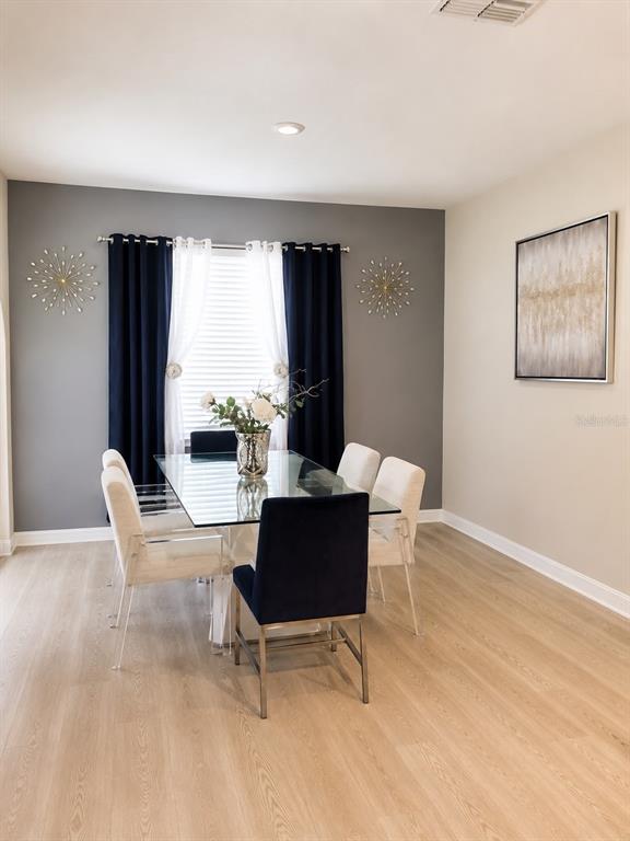 A dining room features a glass table, navy and white curtains, and light wood flooring — 3653 SCARLET OAK DRIVE, ST CLOUD, FL