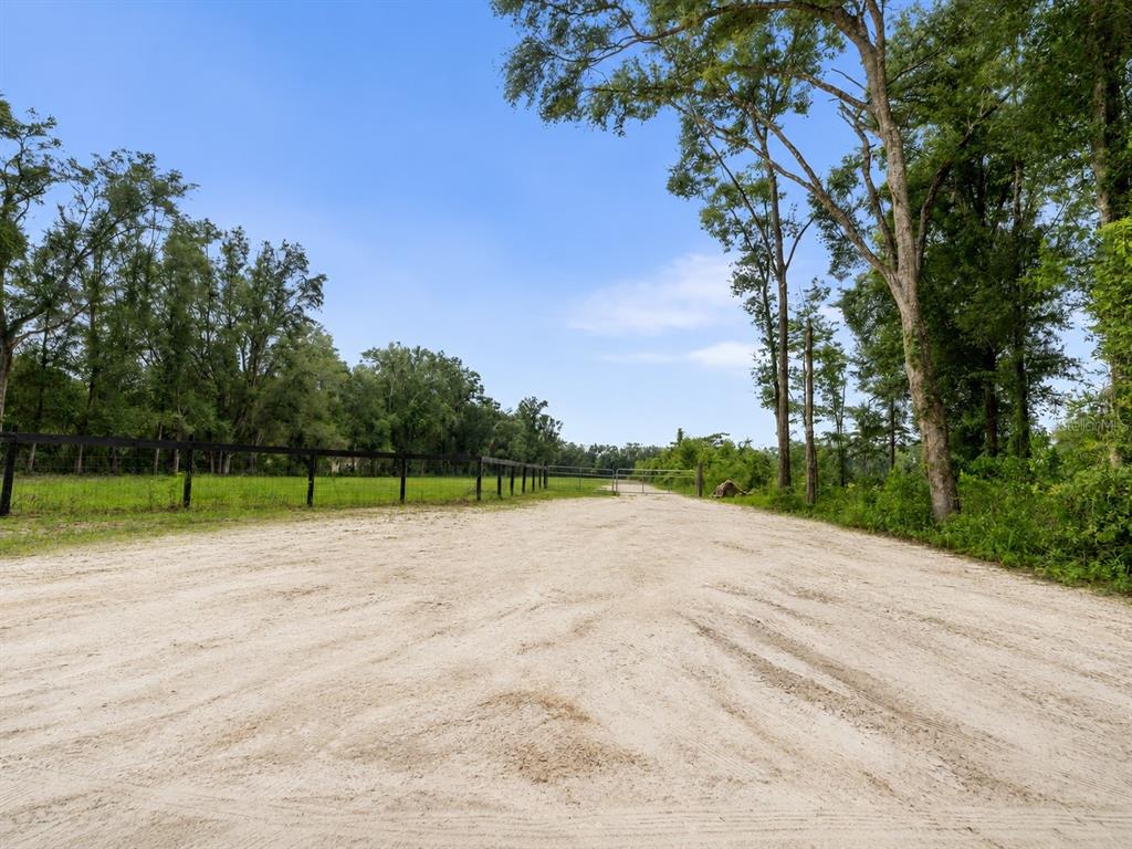 A dirt road runs alongside a fenced, grassy field bordered by tall trees — 17807 SW 83RD AVENUE, ARCHER, FL