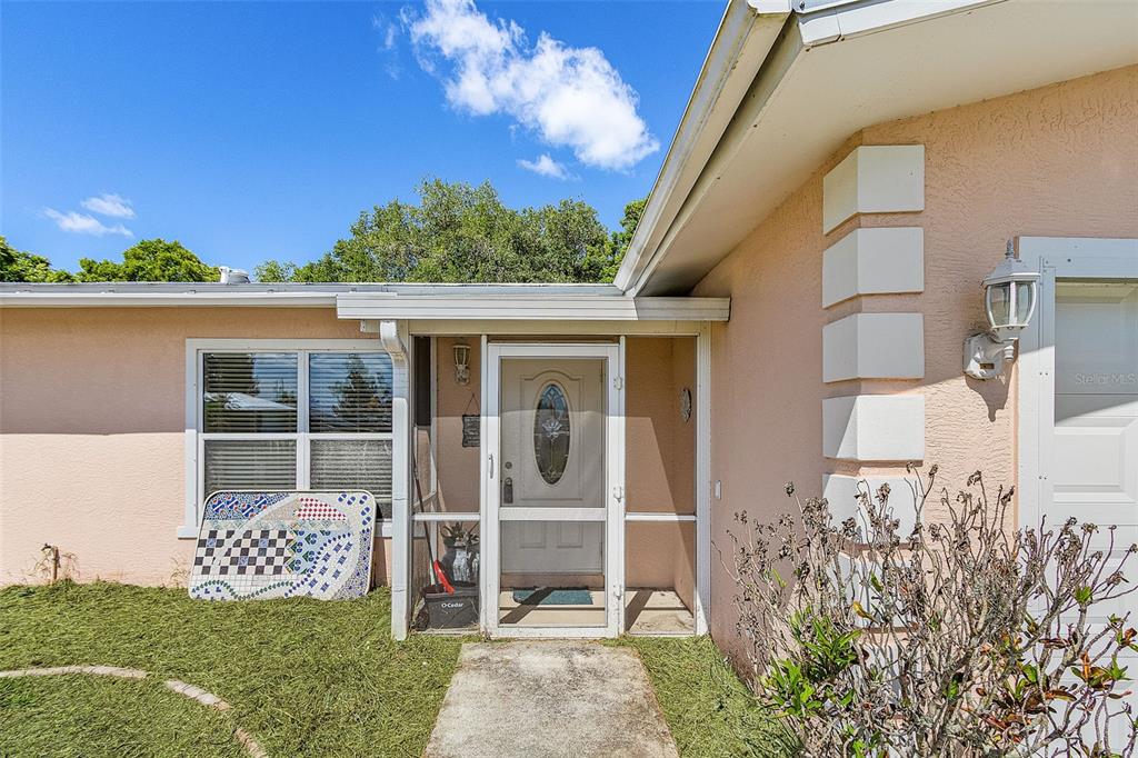The exterior of a peach-colored house features a screened front door and a small walkway — 11337 SW PINE AVENUE, ARCADIA, FL