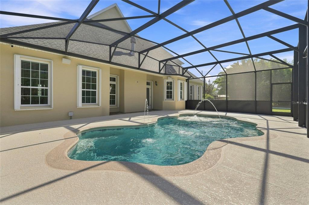 A swimming pool with water features sits inside a screened-in patio behind a beige house — 4441 DEER RUN ROAD, ST CLOUD, FL
