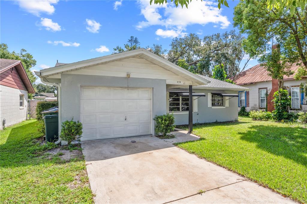 A single-story house with a white garage door, concrete driveway, and a grassy front yard — 519 MASSACHUSETTS AVENUE, ST CLOUD, FL