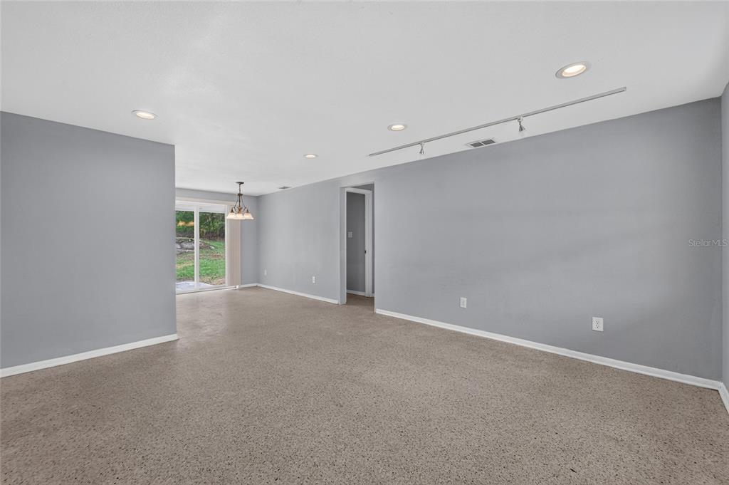 An empty living room with gray walls, carpeted flooring, recessed lighting, and a sliding glass door — 506 SHAMROCK ROAD, BRANDON, FL
