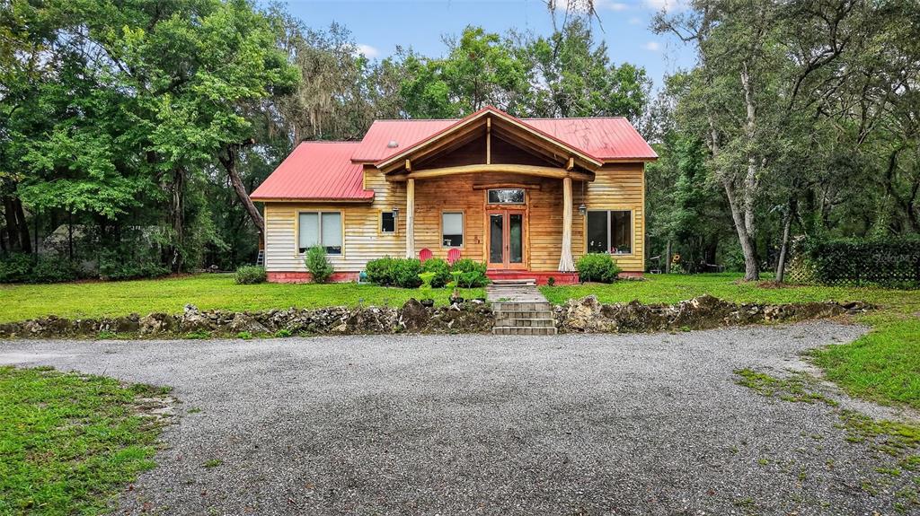 A rustic wooden house with a red metal roof sits behind a gravel driveway — 1862 S US 301, SUMTERVILLE, FL