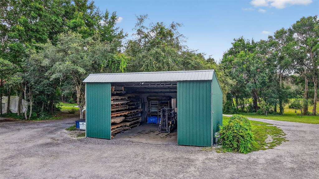 A green metal storage shed sits on a gravel lot surrounded by trees — 1862 S US 301, SUMTERVILLE, FL