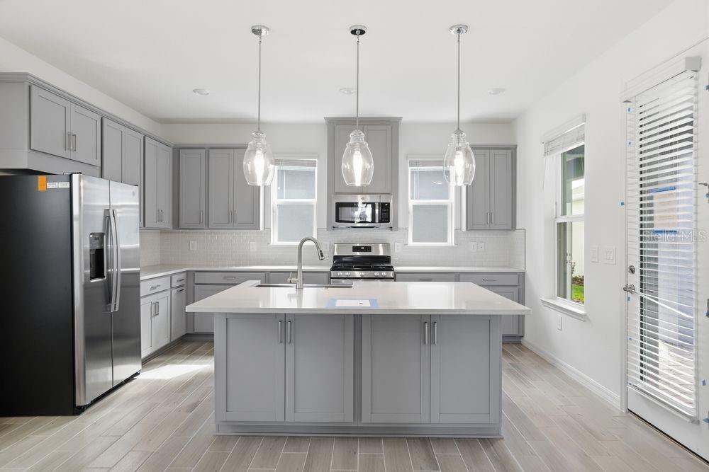 A modern kitchen features gray cabinetry, a central island with a sink, and stainless appliances — 16050 HONEY HARVEST STREET, WINTER GARDEN, FL