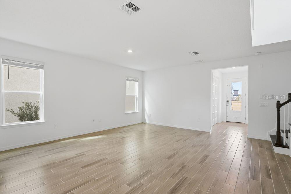 An empty living room features light-colored wood-look tile flooring, white walls, and a front entryway — 16050 HONEY HARVEST STREET, WINTER GARDEN, FL