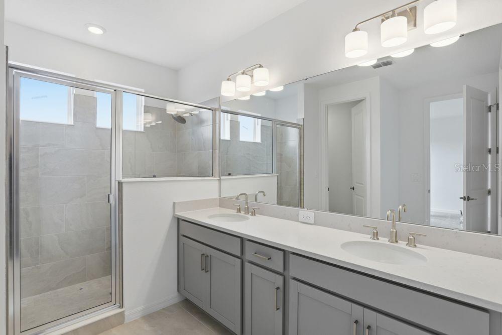 A bathroom features a double vanity with gray cabinets, a large mirror, and a glass shower — 16050 HONEY HARVEST STREET, WINTER GARDEN, FL