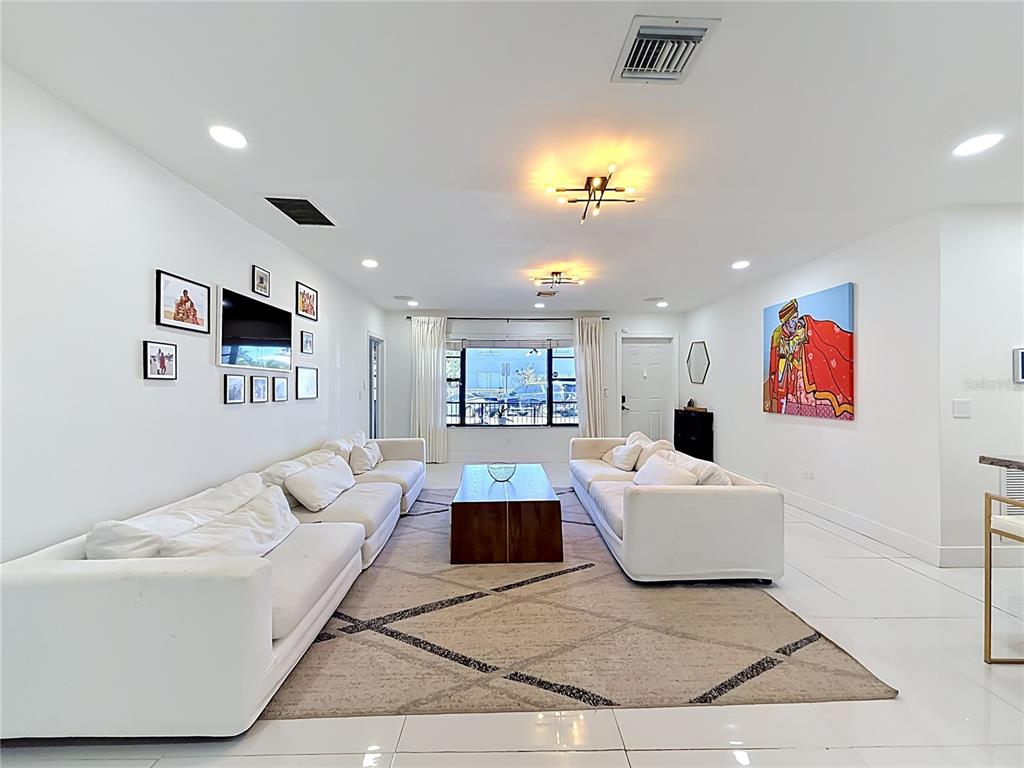 A bright, open-concept living room features white tile floors, white sofas, and a large television — 821 83RD ST, MIAMI BEACH, FL