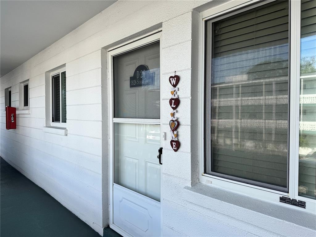A white exterior wall features a screen door, a window, and a hanging welcome sign — 1826 SUNNY DRIVE UNIT D26, BRADENTON, FL