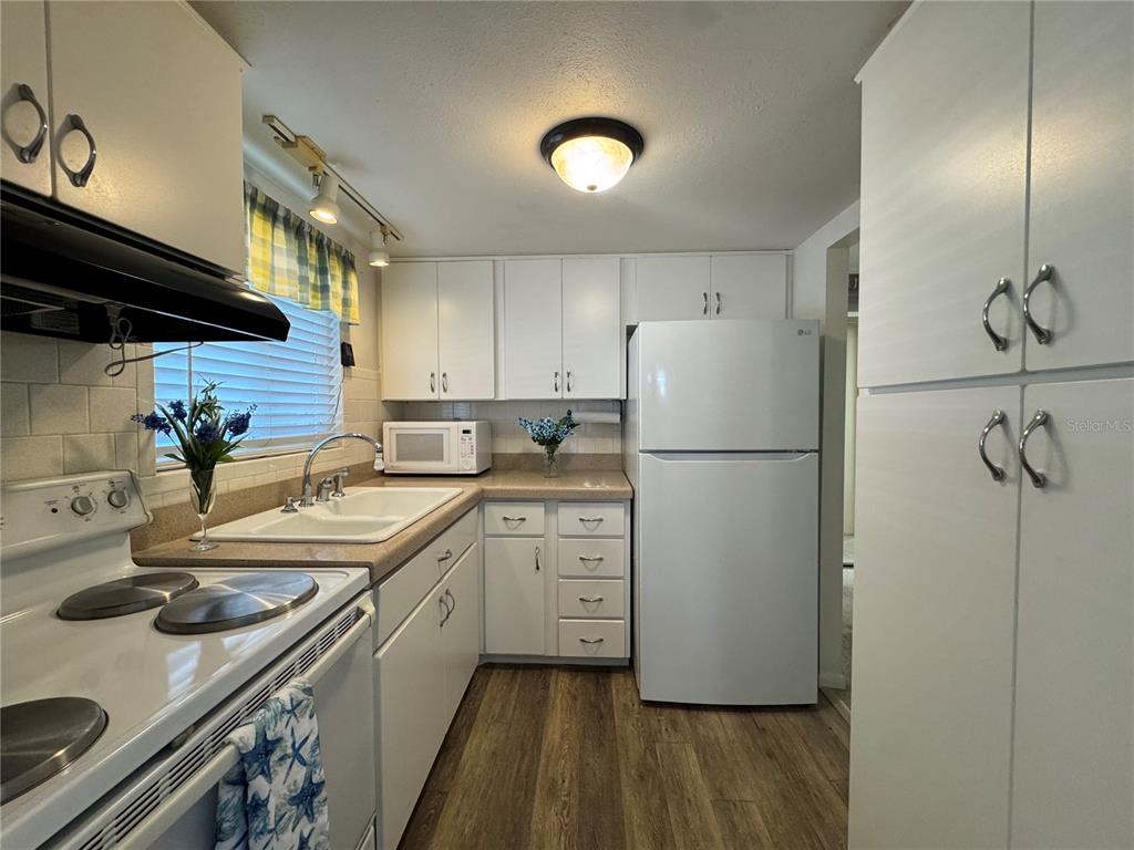 A kitchen features white cabinets, a white refrigerator, a white stove, and wood-look flooring — 1826 SUNNY DRIVE UNIT D26, BRADENTON, FL