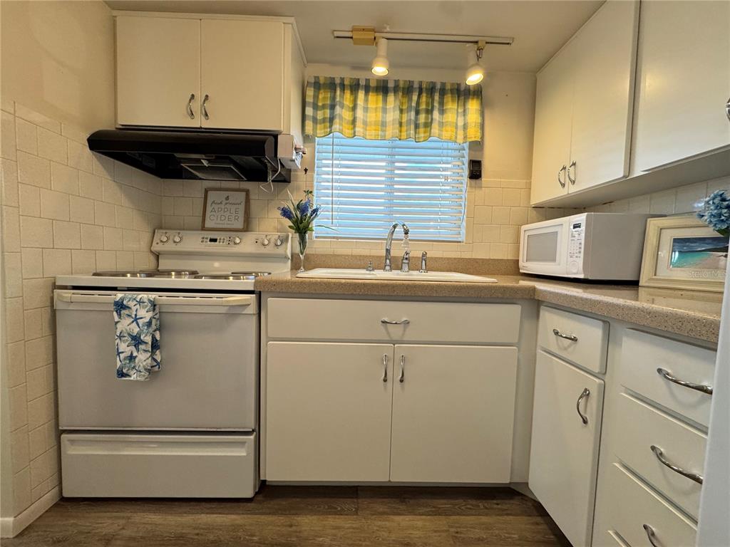 A kitchen features white cabinets, a white stove, a sink, and a tiled backsplash — 1826 SUNNY DRIVE UNIT D26, BRADENTON, FL