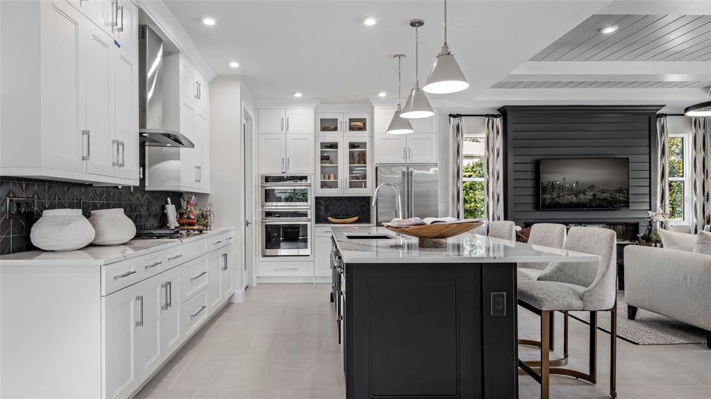 A modern kitchen features white cabinetry, a dark island, and a black shiplap fireplace wall — 1732 POINT GRACE ROAD, TAVARES, FL