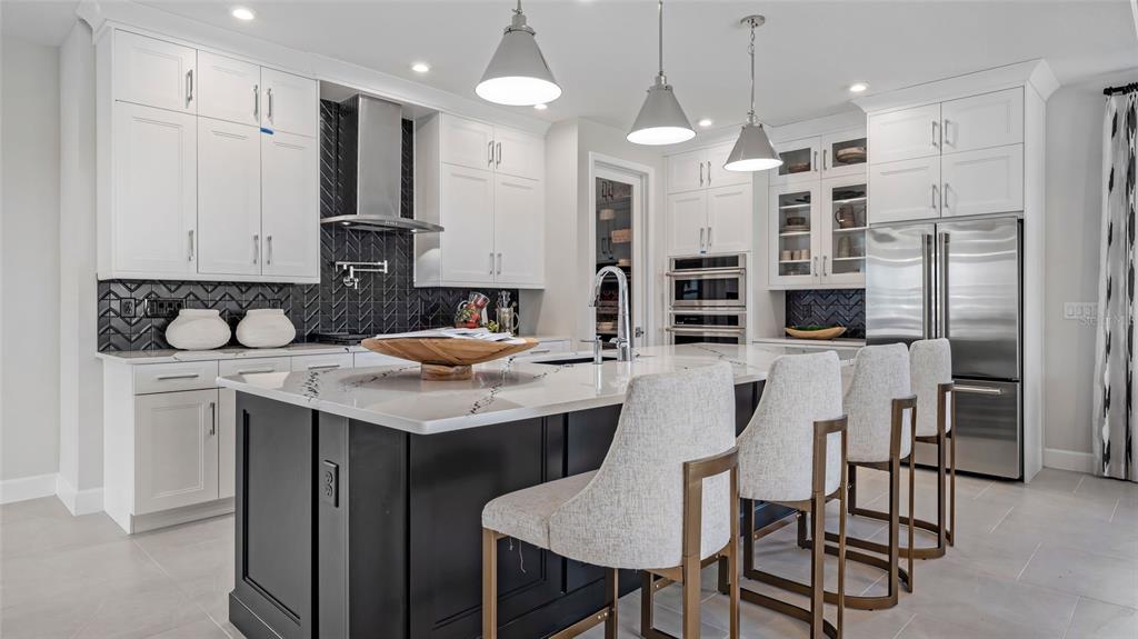 A modern kitchen features a black island with bar stools, white cabinetry, and dark backsplash — 1732 POINT GRACE ROAD, TAVARES, FL