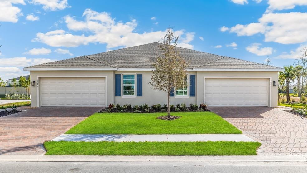 A single-story duplex with two garages, blue shutters, and a central tree in the front yard — 9563 SUNBEAM CIRCLE, PUNTA GORDA, FL