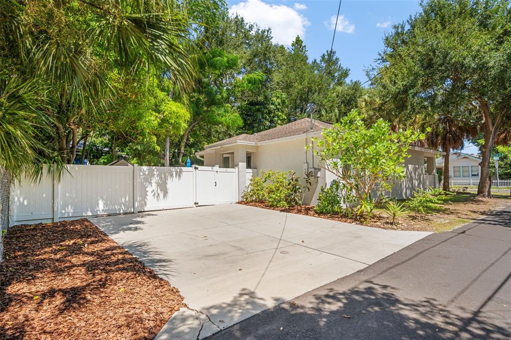 A concrete driveway leads to a white fenced gate beside a single-story house with trees — 325 WISCONSIN COURT S, ST PETERSBURG, FL