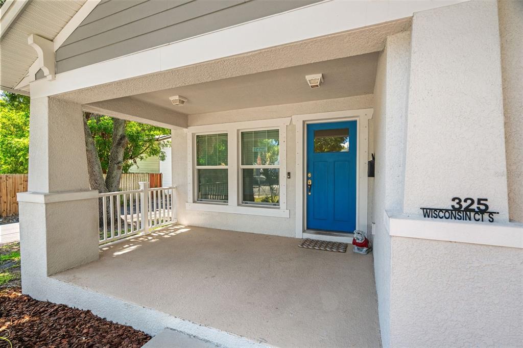 A covered front porch with a blue door, white railings, and a concrete floor — 325 WISCONSIN COURT S, ST PETERSBURG, FL