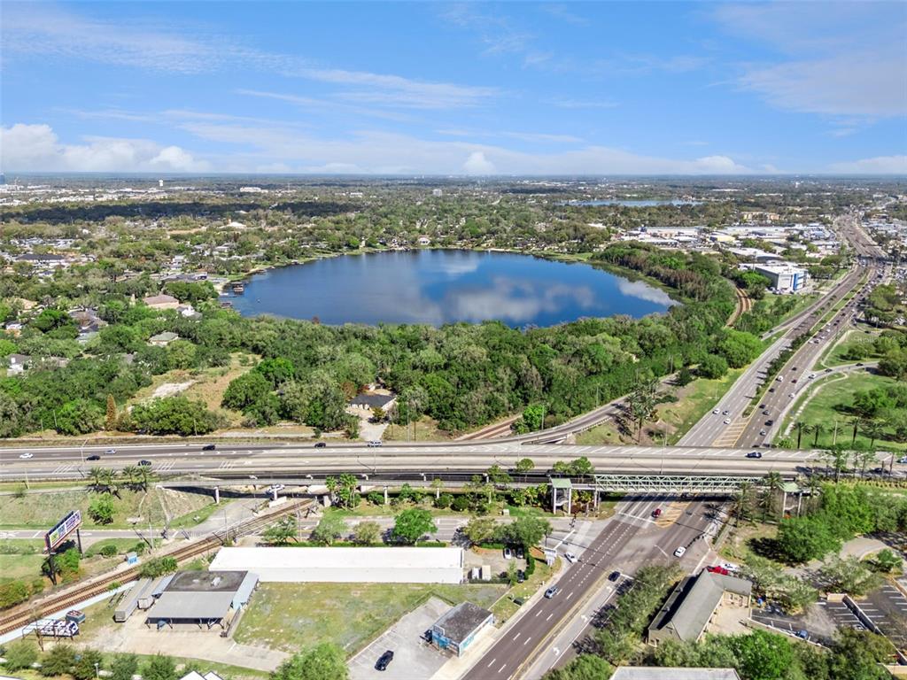 An aerial view shows a lake surrounded by trees, a highway overpass, and nearby buildings — MECHANIC STREET, MAITLAND, FL