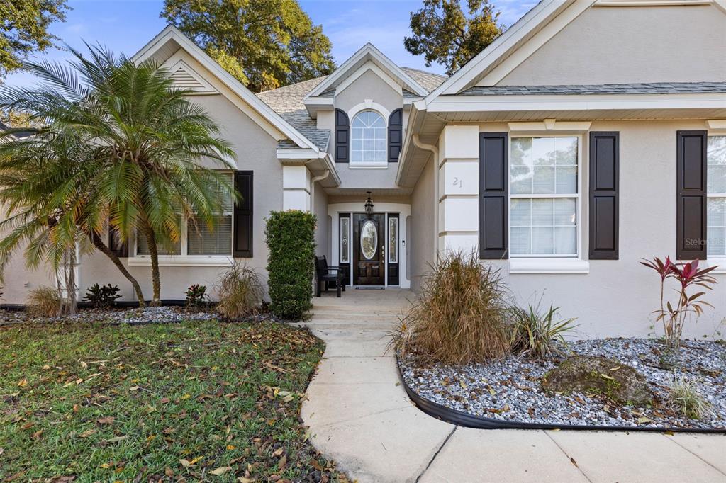 A single-story house with a beige stucco exterior, dark shutters, and a palm tree — 21 WHITEHALL COURT, FLAGLER BEACH, FL
