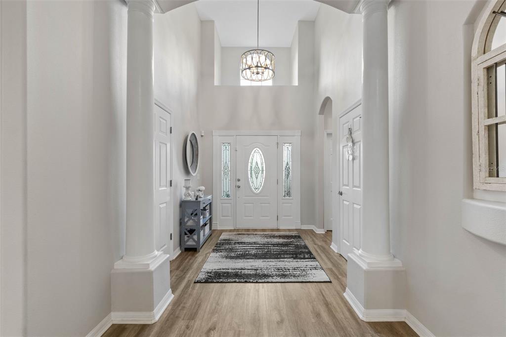 A bright foyer features white columns, a high ceiling with a chandelier, and wood flooring — 21 WHITEHALL COURT, FLAGLER BEACH, FL