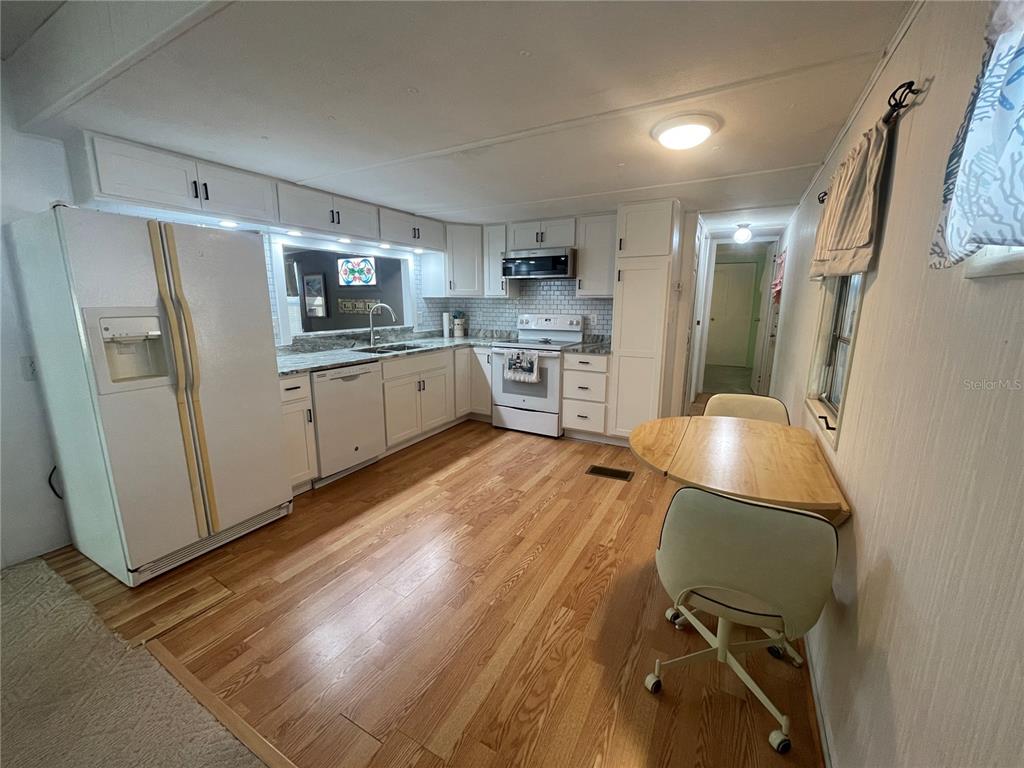 A kitchen features white cabinets, stainless steel appliances, wood flooring, and a small dining area — 504 49TH C AVENUE DRIVE E, BRADENTON, FL