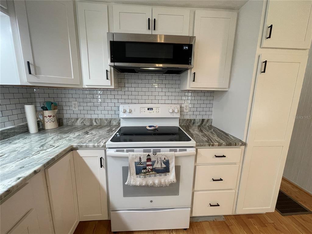 A kitchen features white cabinets, a stainless steel microwave, a white stove, and subway tile — 504 49TH C AVENUE DRIVE E, BRADENTON, FL