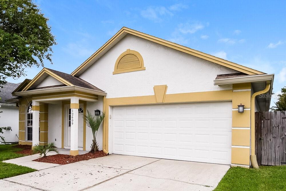 A single-story house with a white stucco exterior, yellow trim, and a two-car garage — 12609 WHITERAPIDS DRIVE, ORLANDO, FL