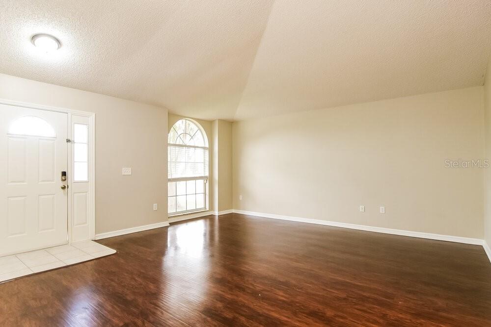 An empty room with dark wood flooring, beige walls, a white front door, and arched window — 12609 WHITERAPIDS DRIVE, ORLANDO, FL