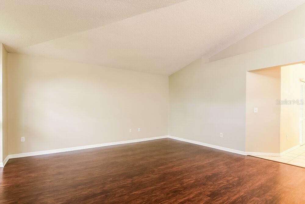 An empty room with light-colored walls, a vaulted ceiling, and dark wood-look flooring — 12609 WHITERAPIDS DRIVE, ORLANDO, FL