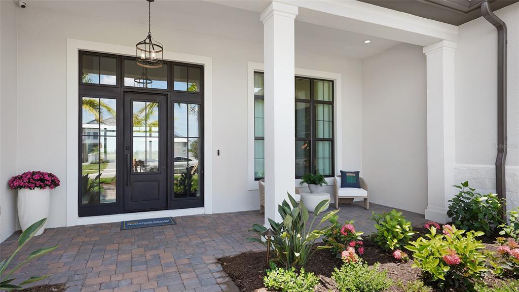 A covered front porch features a dark-framed glass door, white columns, and paver flooring — 11433 BRIGHTLY DRIVE, VENICE, FL