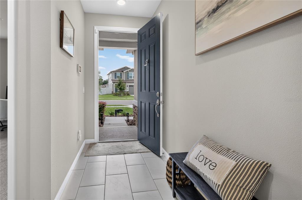 A bright entryway features gray tile flooring, a dark blue front door, and a bench — 3625 SUBLETT LOOP, TAVARES, FL