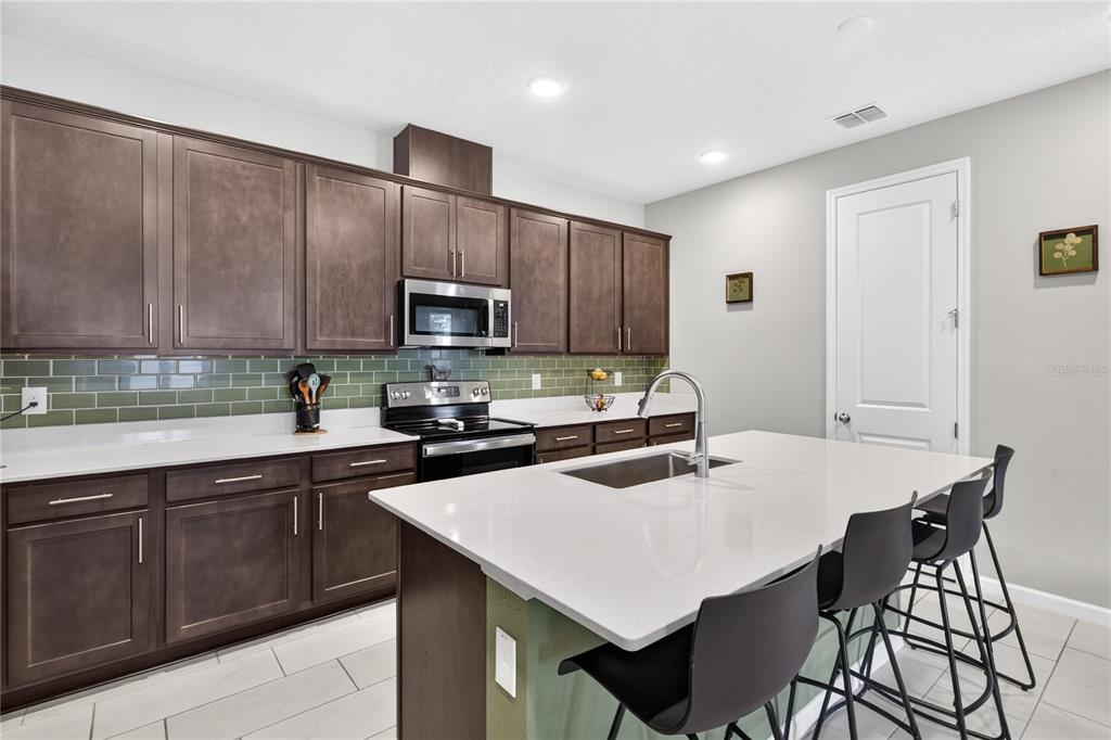A kitchen featuring dark wood cabinets, a white quartz island, and a green subway tile backsplash — 3625 SUBLETT LOOP, TAVARES, FL