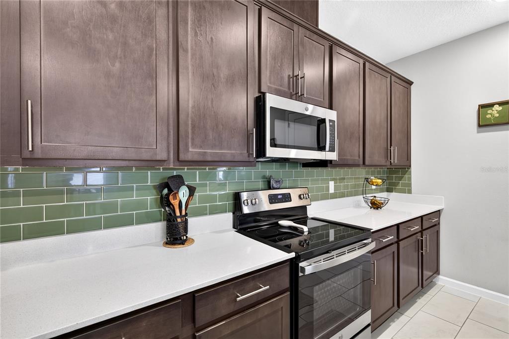 A kitchen features dark wood cabinets, a green subway tile backsplash, and stainless steel appliances — 3625 SUBLETT LOOP, TAVARES, FL
