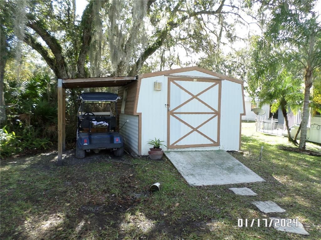 A white storage shed with a brown-trimmed door and an attached golf cart carport — 76 NW ROAN ROAD, RIVER RANCH, FL