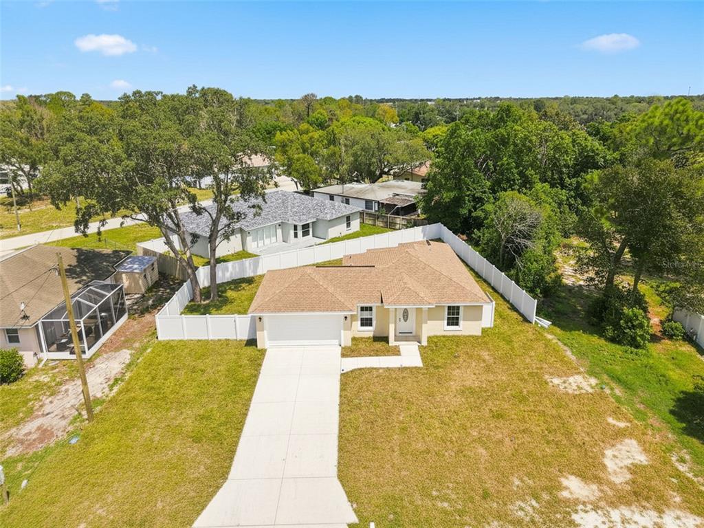 A single-story yellow house with a two-car garage and white vinyl fencing under a blue sky — 7209 APACHE TRAIL, SPRING HILL, FL