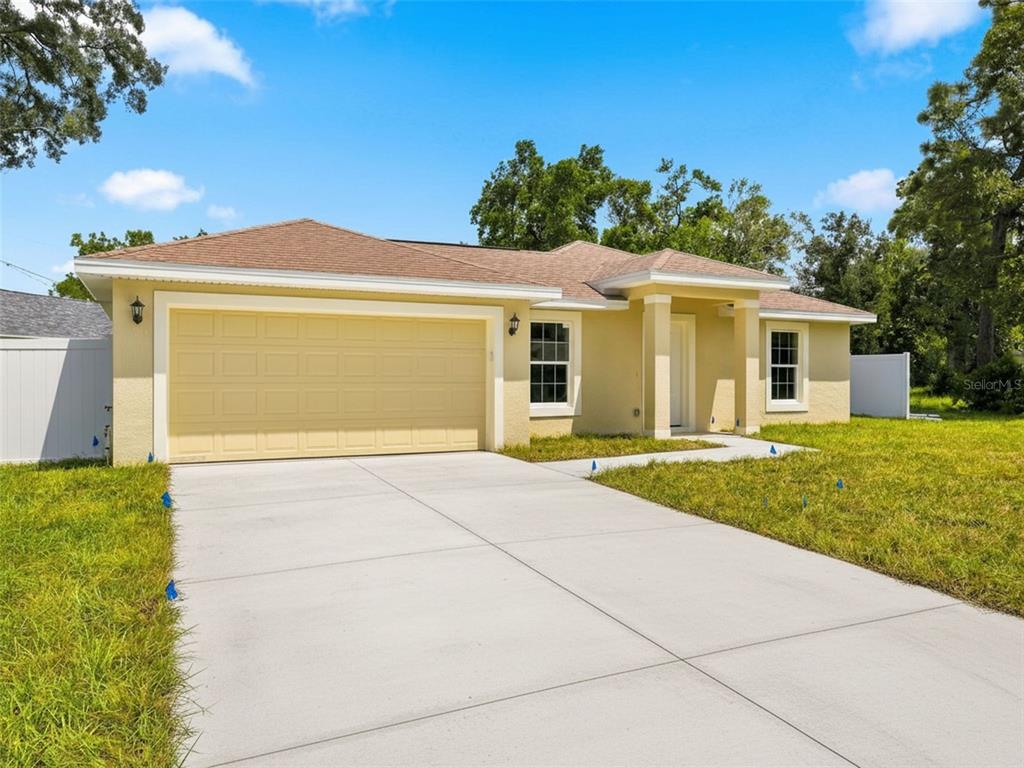 A single-story yellow house with a two-car garage and a concrete driveway — 7209 APACHE TRAIL, SPRING HILL, FL