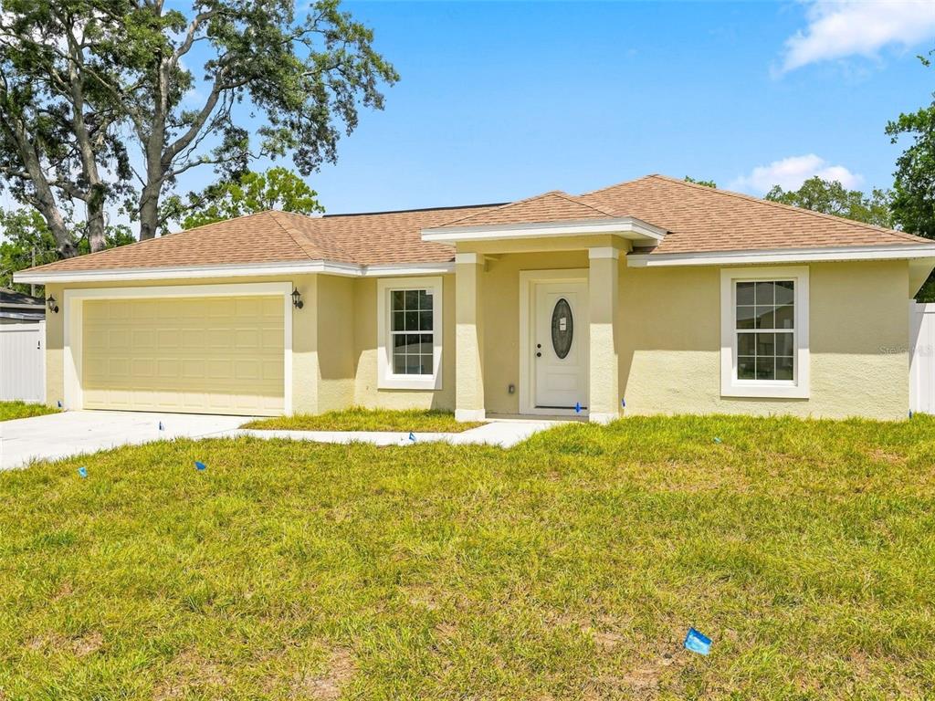 A single-story house with a yellow stucco exterior, a two-car garage, and a covered entryway — 7209 APACHE TRAIL, SPRING HILL, FL