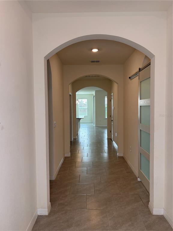 A hallway with light-colored walls, tiled floors, and arched transitions leads to another room — 6930 AUDOBON OSPREY COVE, HARMONY, FL