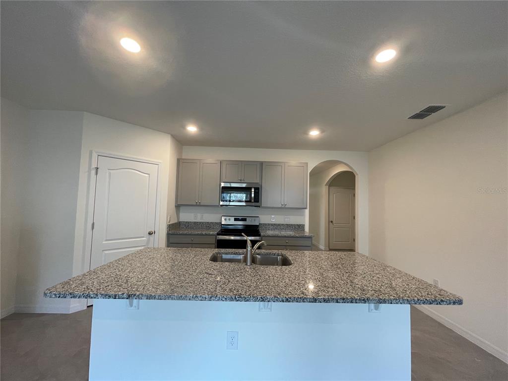 A kitchen features a granite-topped island, gray cabinetry, stainless steel appliances, and recessed lighting — 5610 GALLOPING DRIVE, APOPKA, FL
