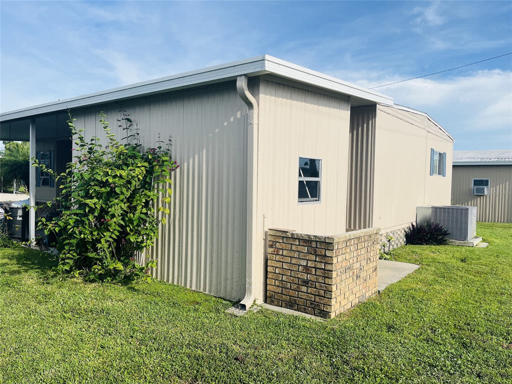 The exterior of a light-colored mobile home features a brick privacy wall and metal siding — 3153 ORCHARD DRIVE, NORTH FORT MYERS, FL
