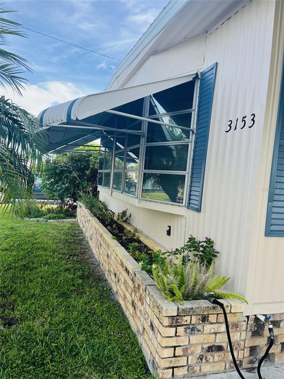 The exterior of a mobile home features a brick planter box and a metal window awning — 3153 ORCHARD DRIVE, NORTH FORT MYERS, FL