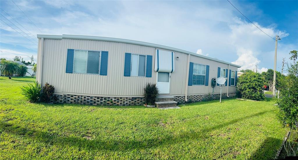 A single-story manufactured home with beige siding, blue shutters, and a brick-patterned skirting — 3153 ORCHARD DRIVE, NORTH FORT MYERS, FL