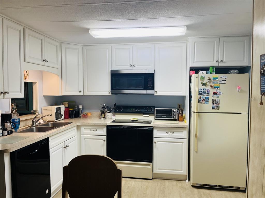 A kitchen features white cabinets, a black stove and dishwasher, and a light-colored refrigerator — 3153 ORCHARD DRIVE, NORTH FORT MYERS, FL