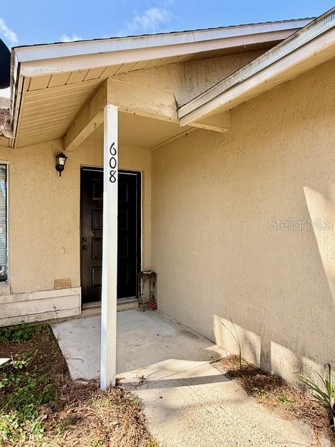 A covered entryway features a dark front door and a white post displaying the number 608 — 608 E WARREN AVENUE, LONGWOOD, FL
