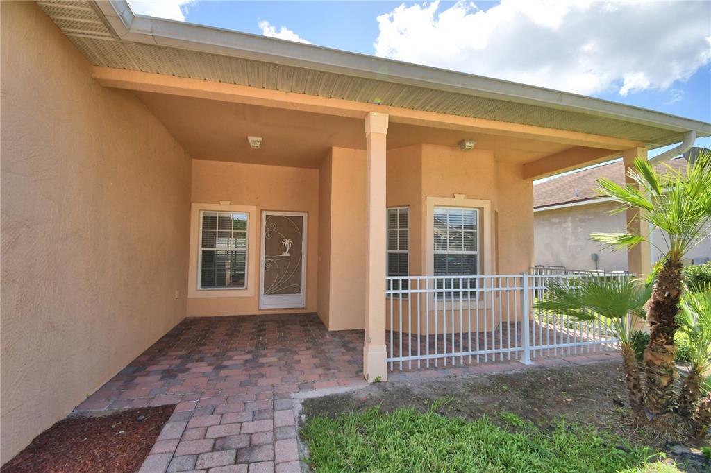 A covered patio features brick pavers, a white metal fence, and a glass storm door — 2338 SALZBURG LOOP, WINTER HAVEN, FL